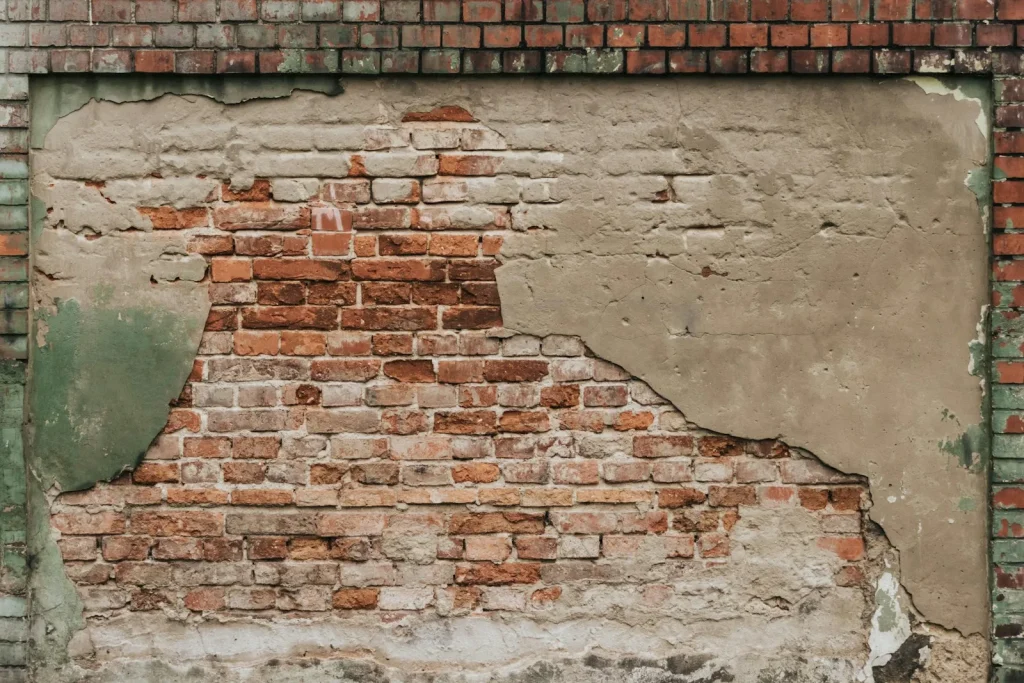 Brick wall with failed plaster and damp staining